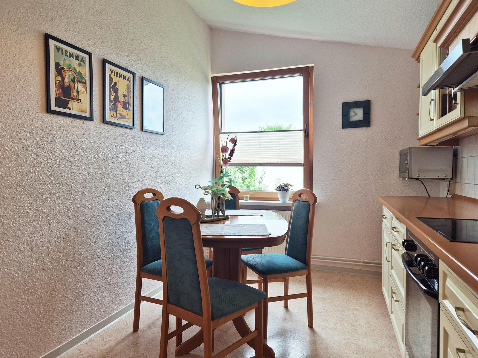Dining area with table, chairs, and kitchen. Wall art and window view.