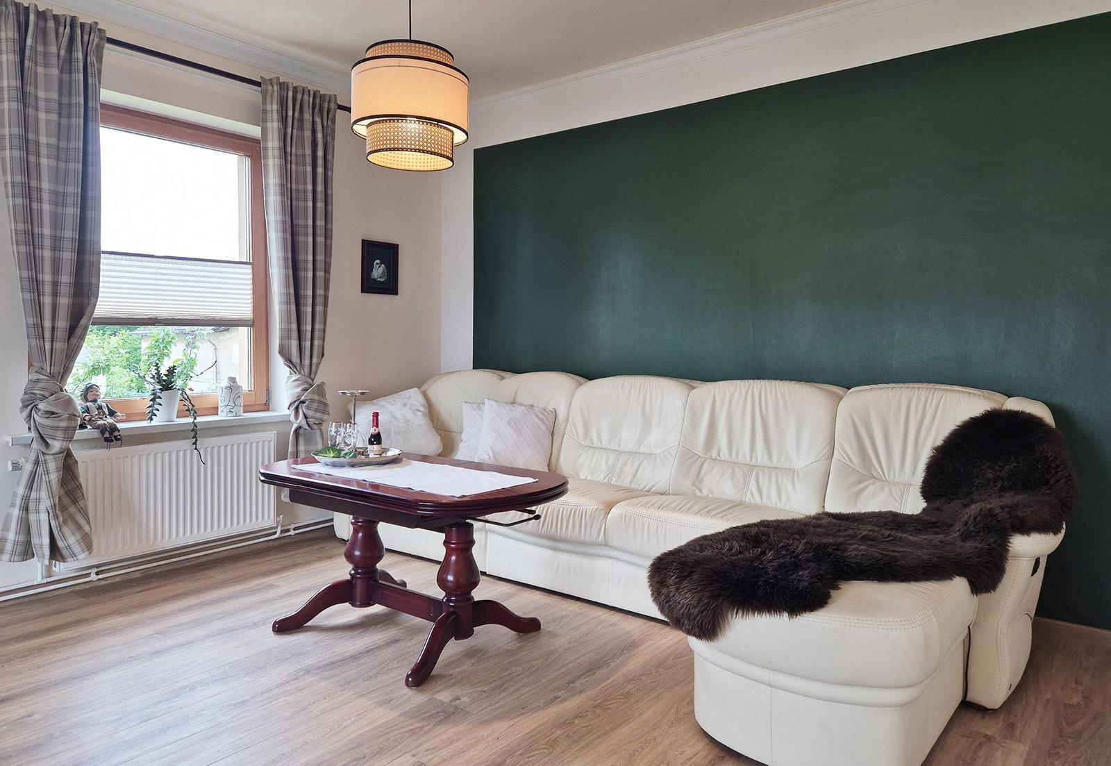 Living room with white sofa, dark green wall panel, and wooden floor.