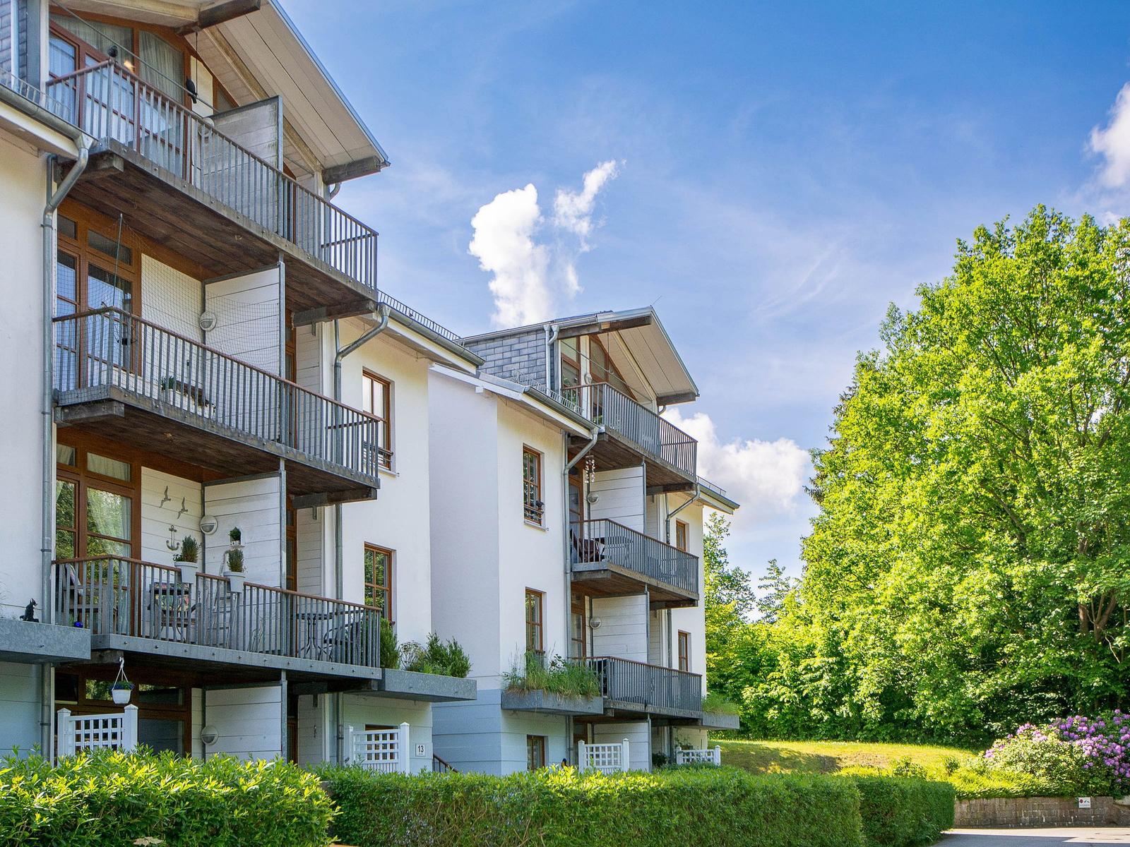 Wohnhaus mit Balkonen und grüner Umgebung unter blauem Himmel.