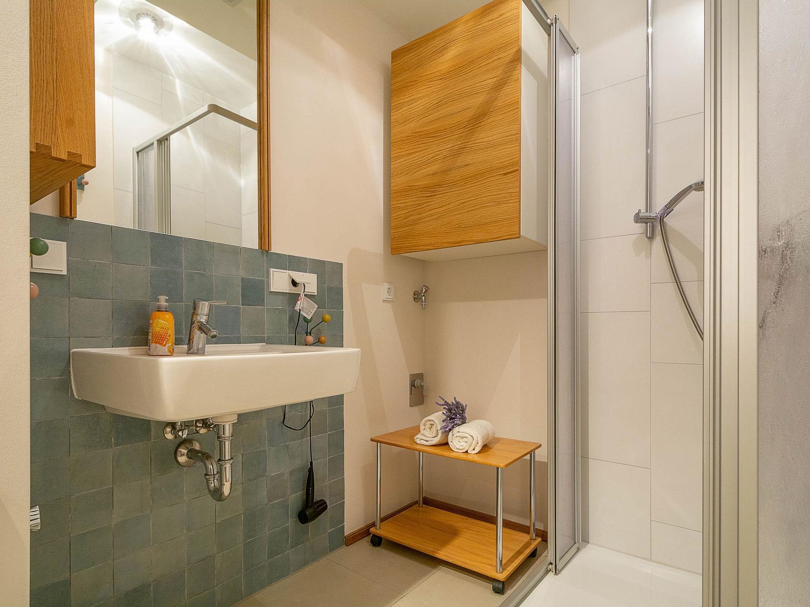 Badezimmer mit Dusche, Waschbecken und Holzschränken.