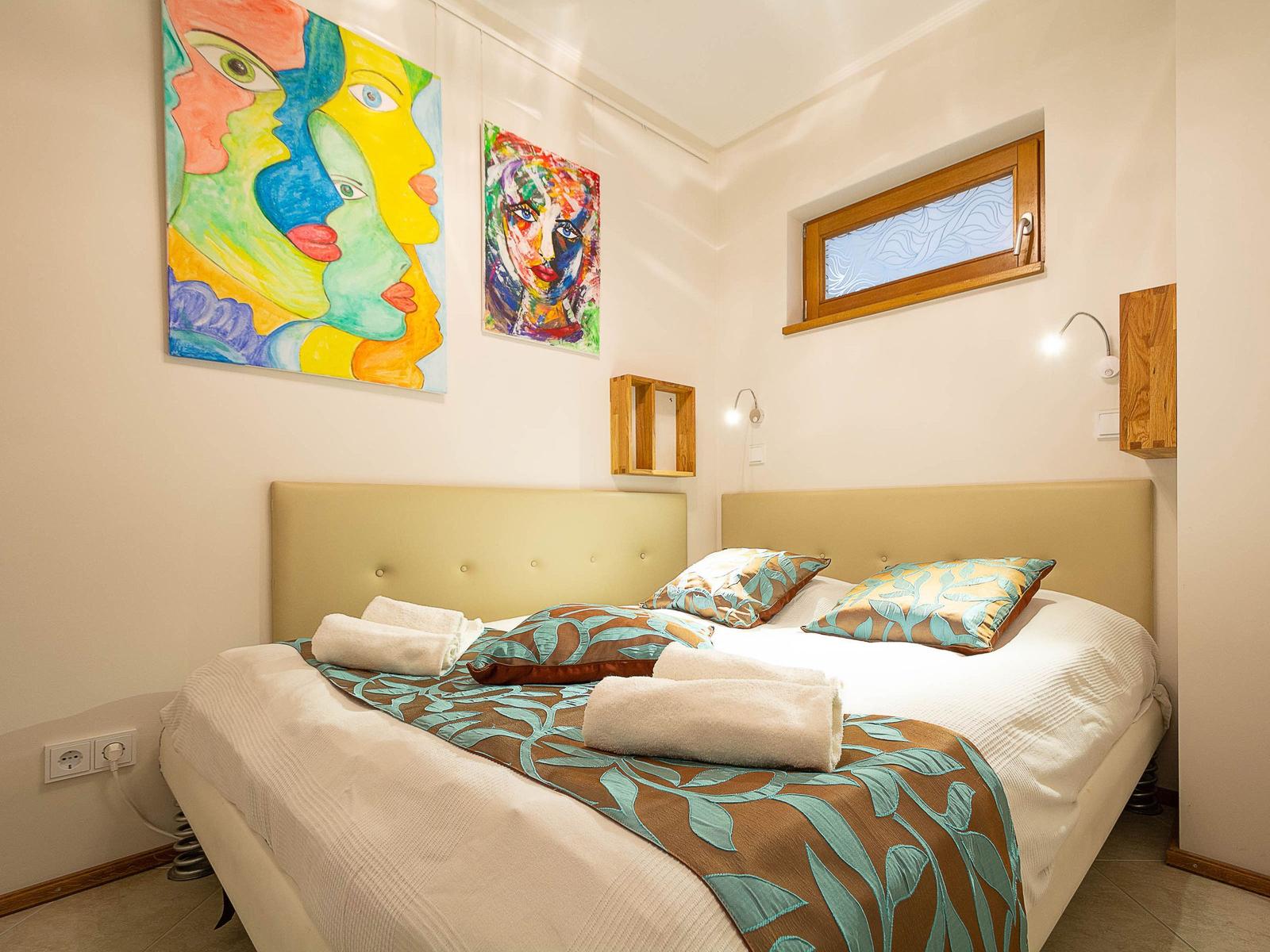 Schlafzimmer mit Bett, Wandkunst und kleinem Fenster.