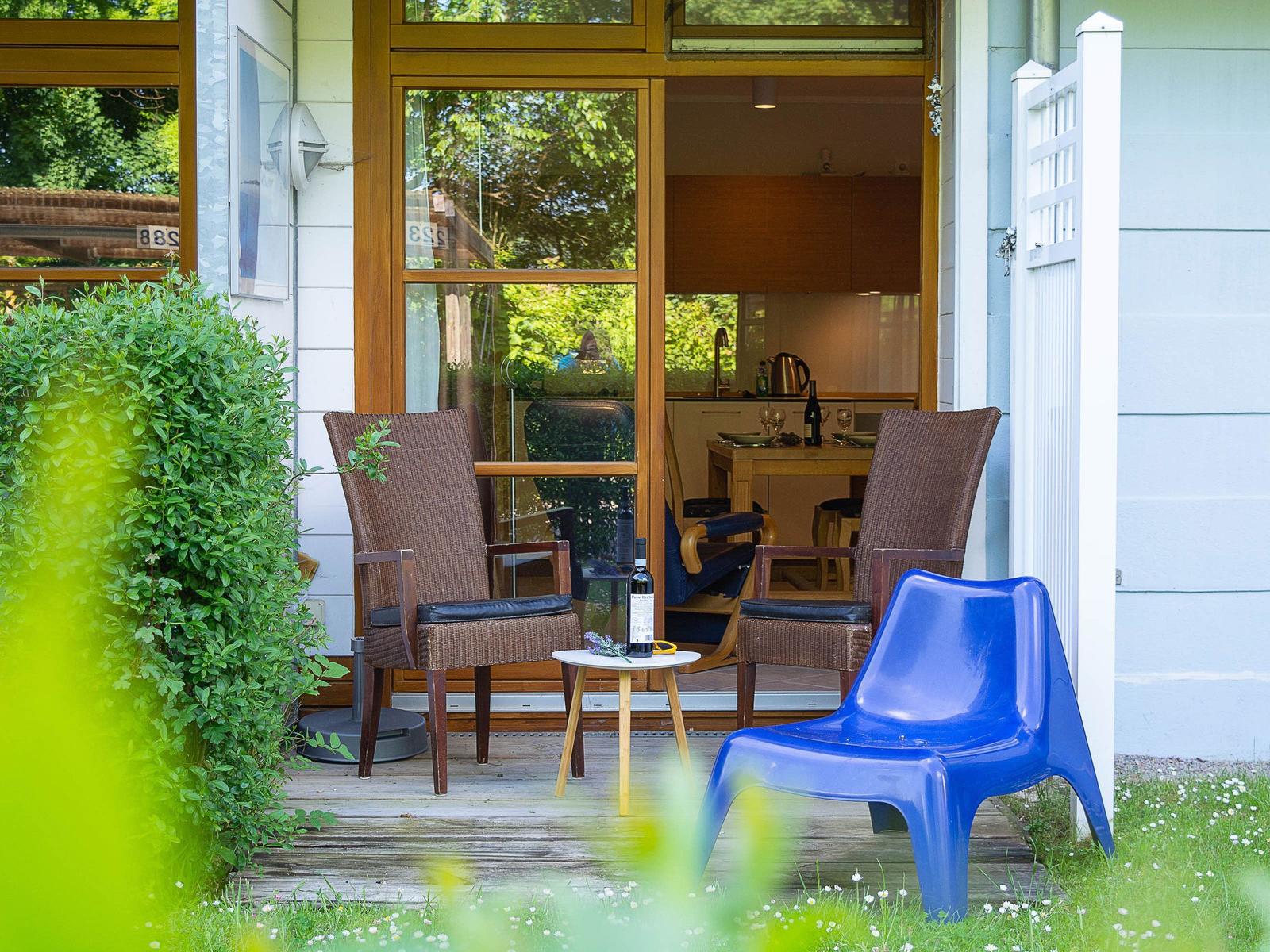 Terrasse mit zwei Stühlen und einem blauen Kunststoffstuhl. Im Hintergrund ist die Küche sichtbar.