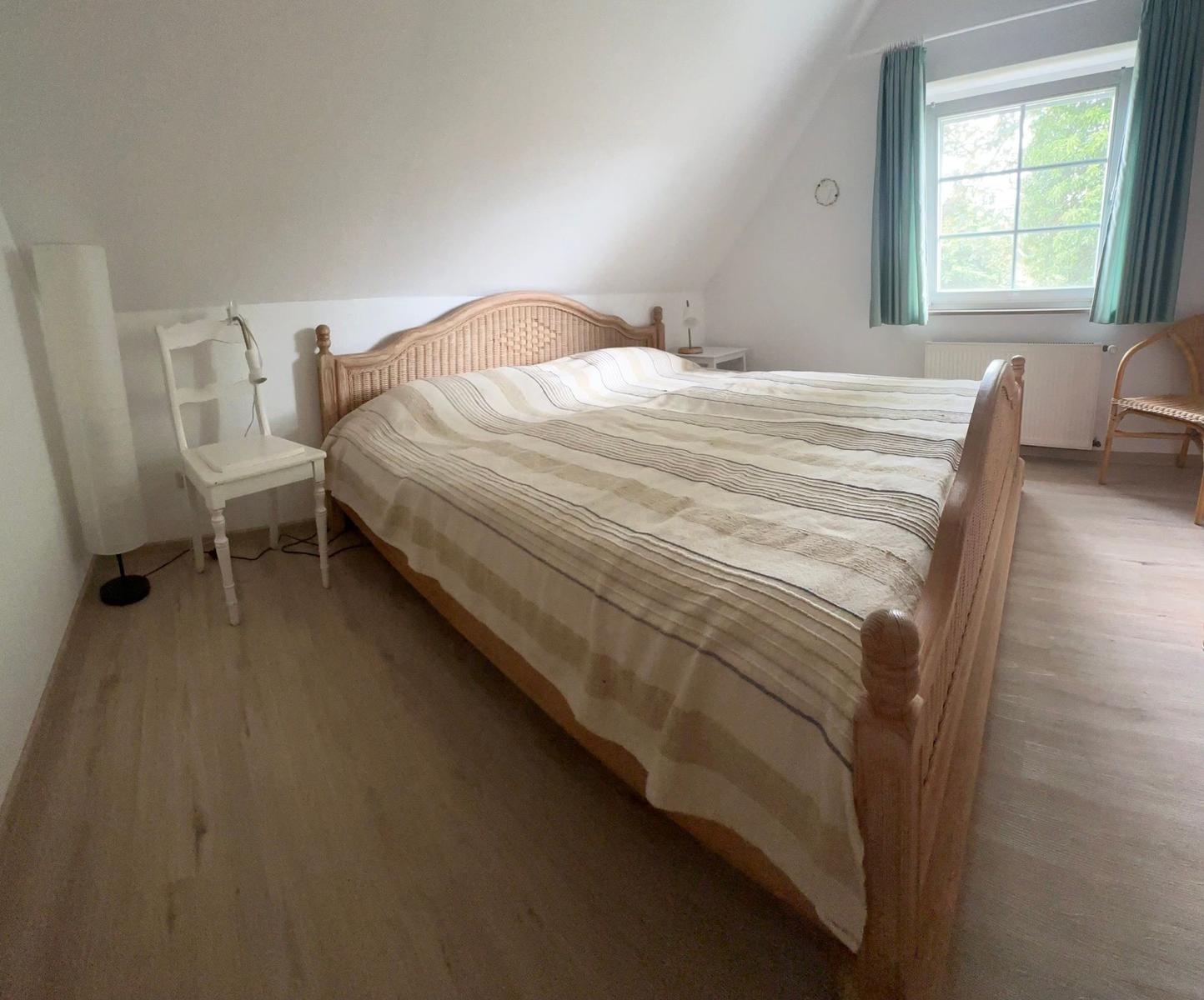 Schlafzimmer mit Doppelbett, Fenster und Holzboden.