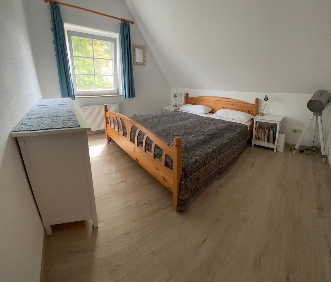 Schlafzimmer mit Holzbett, Fenster und Kleiderschrank.