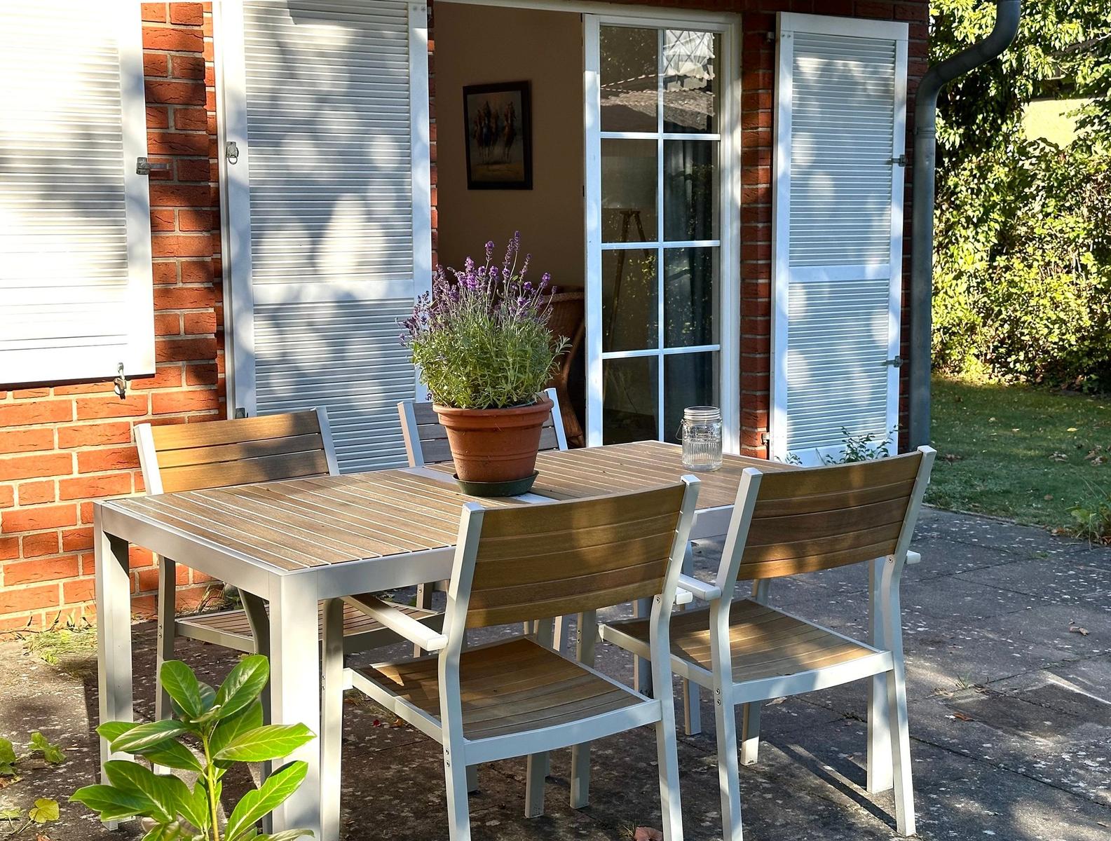 Terrasse mit Tisch und Stühlen, Pflanze und Glasflasche vor Haus mit Fenster und Jalousien.