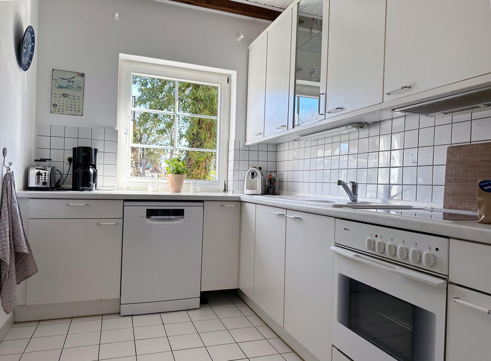 Küche mit weißen Schränken, Spüle, Herd und Fenster mit Blick nach draußen.