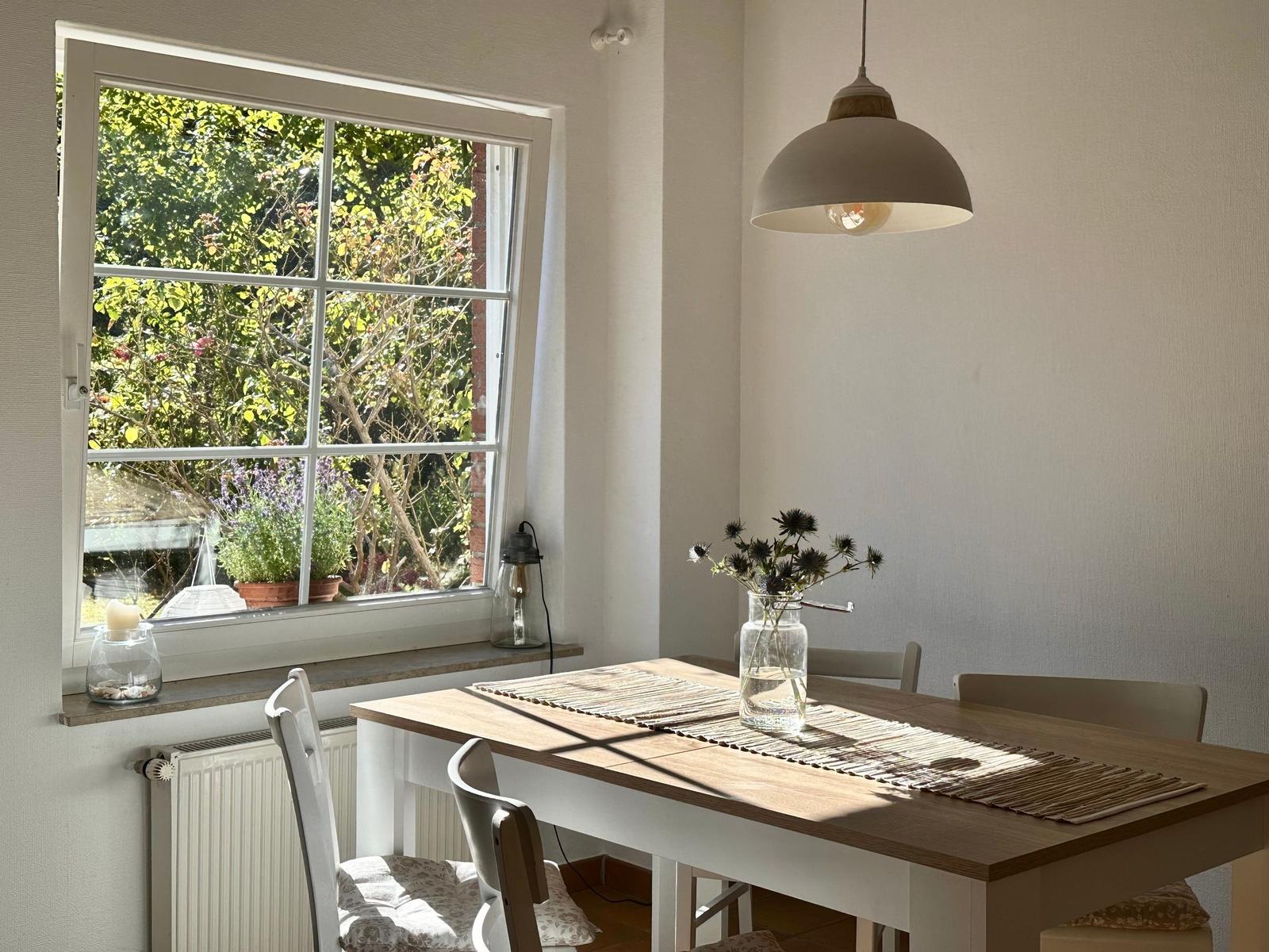 Esstisch mit Stühlen unter einem Hängelampen, Fensterblick auf Garten.