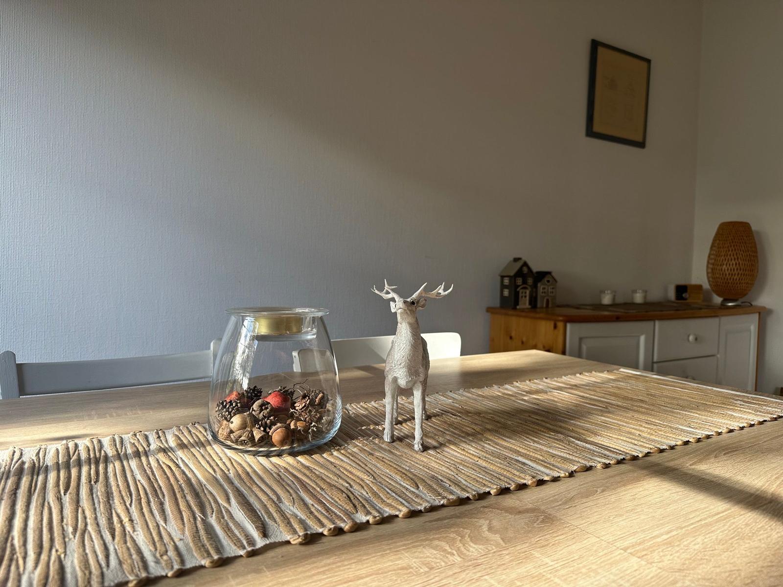 Esstisch mit Deko, Glas mit Nüssen und Hirschfigur auf Bambusläufer.