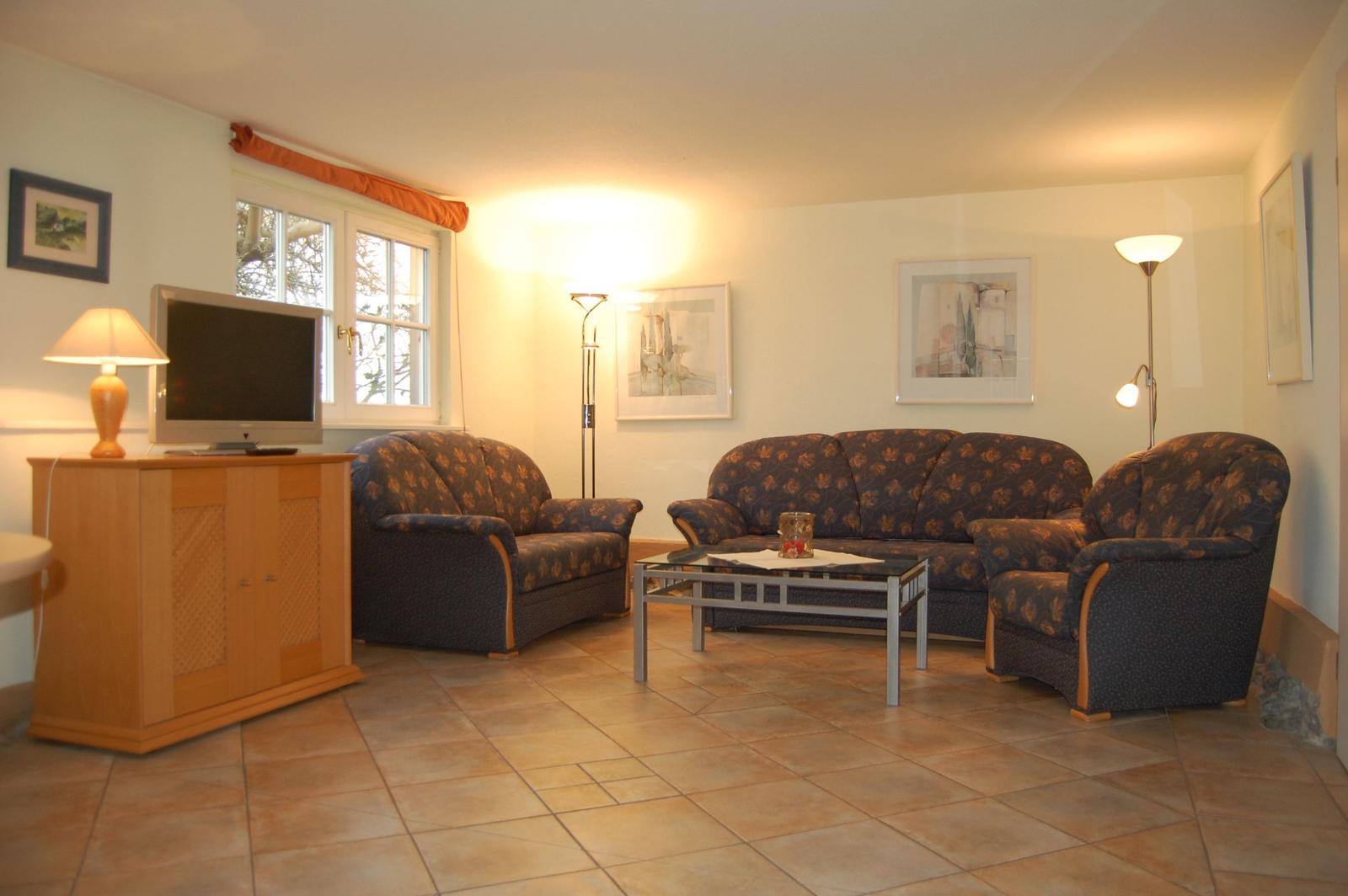 Wohnzimmer mit Sofa, Sesseln, Fernseher und Tisch.