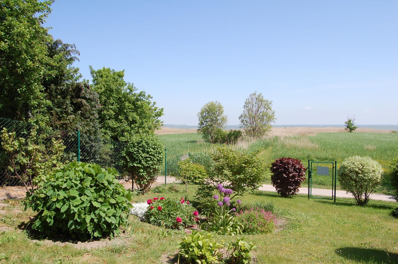Garten mit Blumenbeeten und Zaun. Blick auf Felder und Horizont.