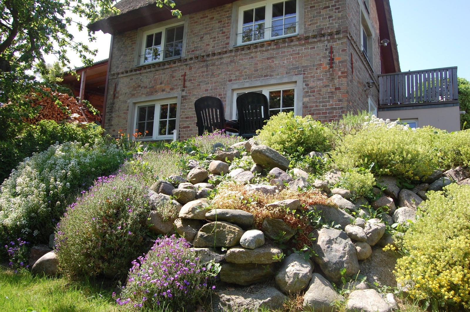 Steinmauer mit Blumen und Sitzgelegenheit vor einem Backsteinhaus