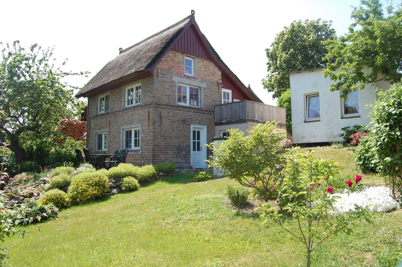 Haus mit Strohdach, Garten und Terrasse. Roter Holzrahmen und weiße Fenster.