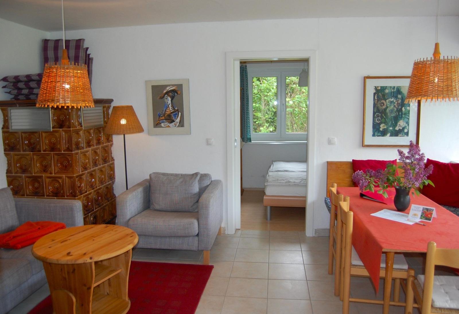 Wohn- und Essbereich mit Blick in Schlafzimmer. Holzmöbel, Wandbilder und Deckenleuchten.