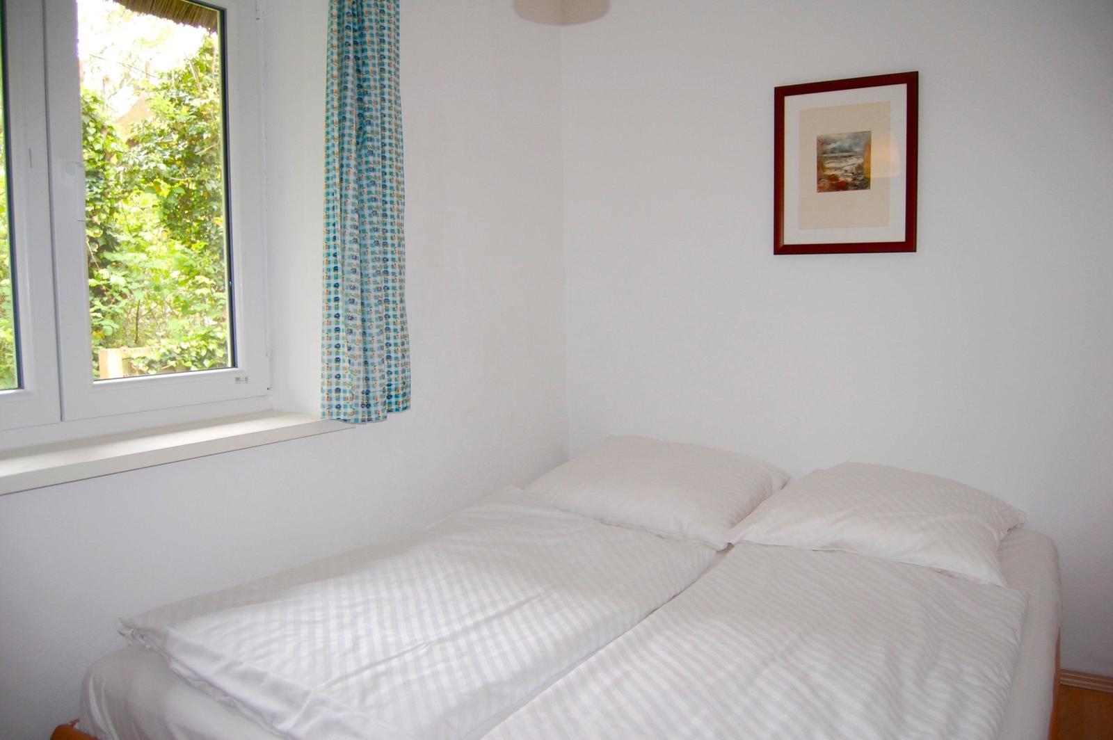 Schlafzimmer mit Doppelbett, Fenster und Bild an der Wand.