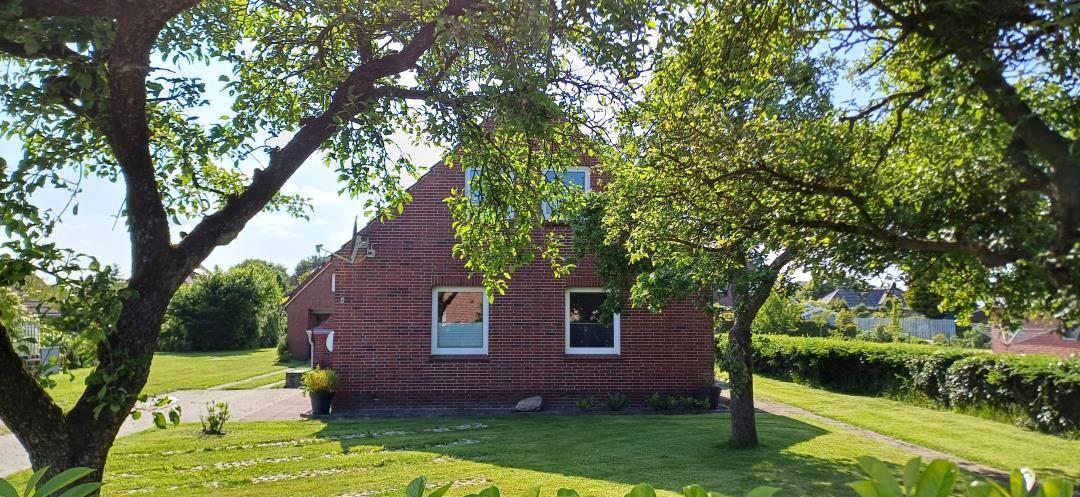 Rotes Backsteingebäude mit grünem Garten und Bäumen im Hintergrund.