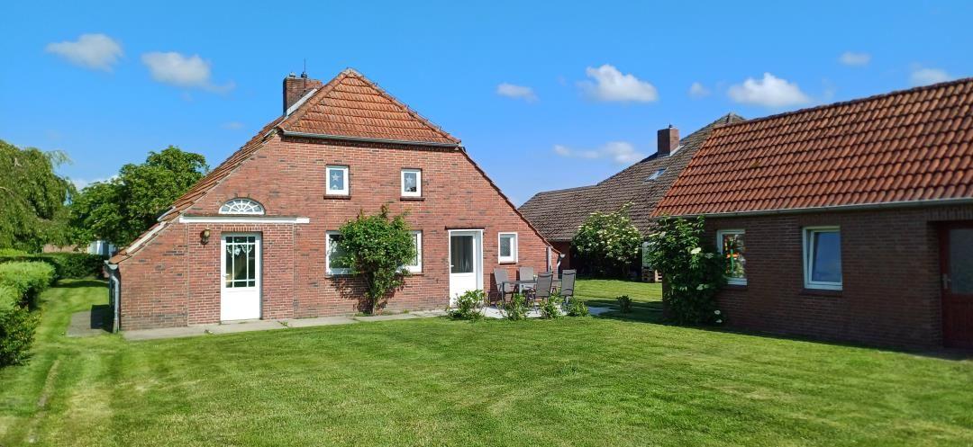 Rotes Backsteingebäude mit Garten und Terrasse unter blauem Himmel.