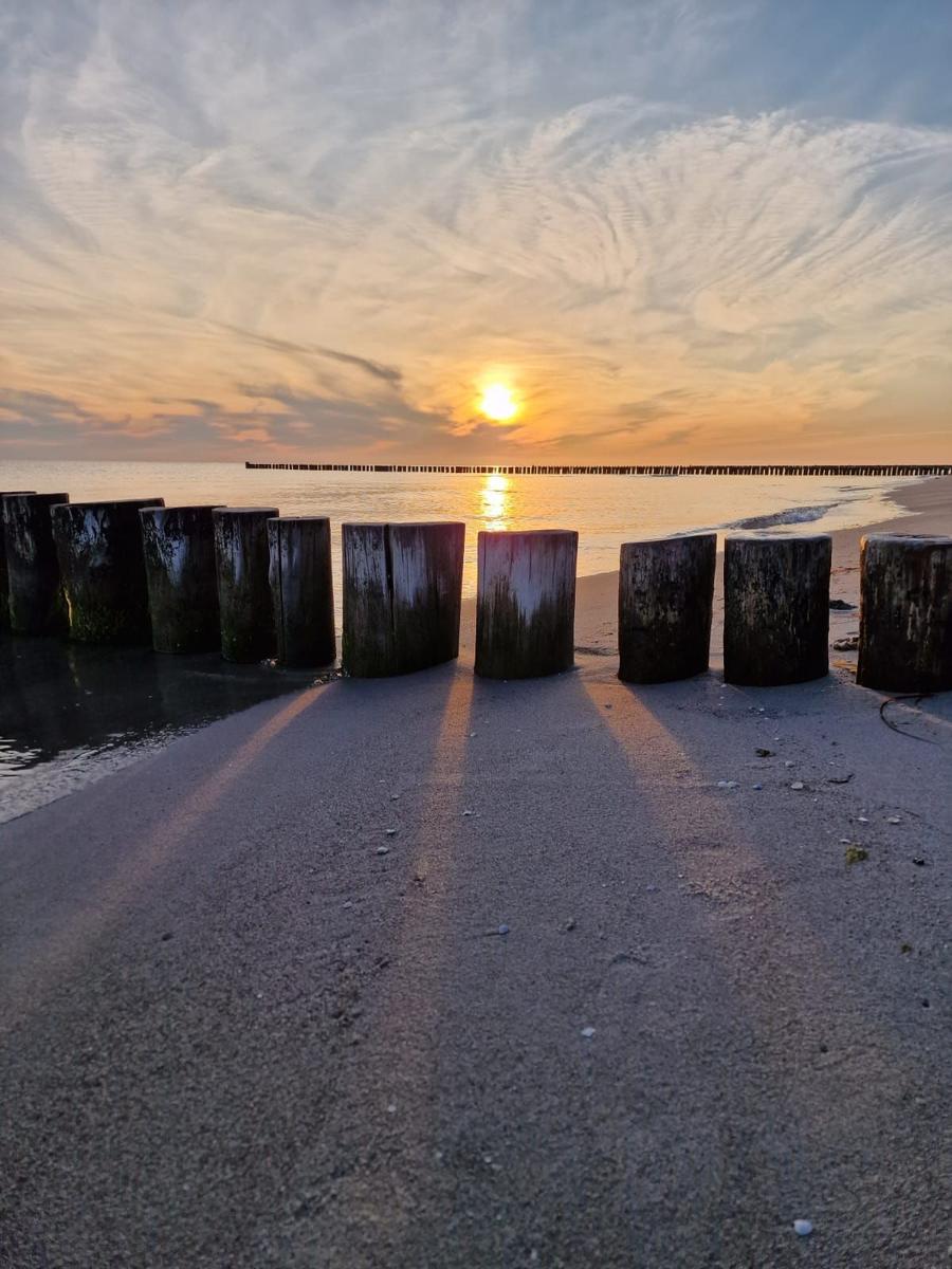 Sonnenuntergang am Strand mit Holzpfählen und Steg im Hintergrund.