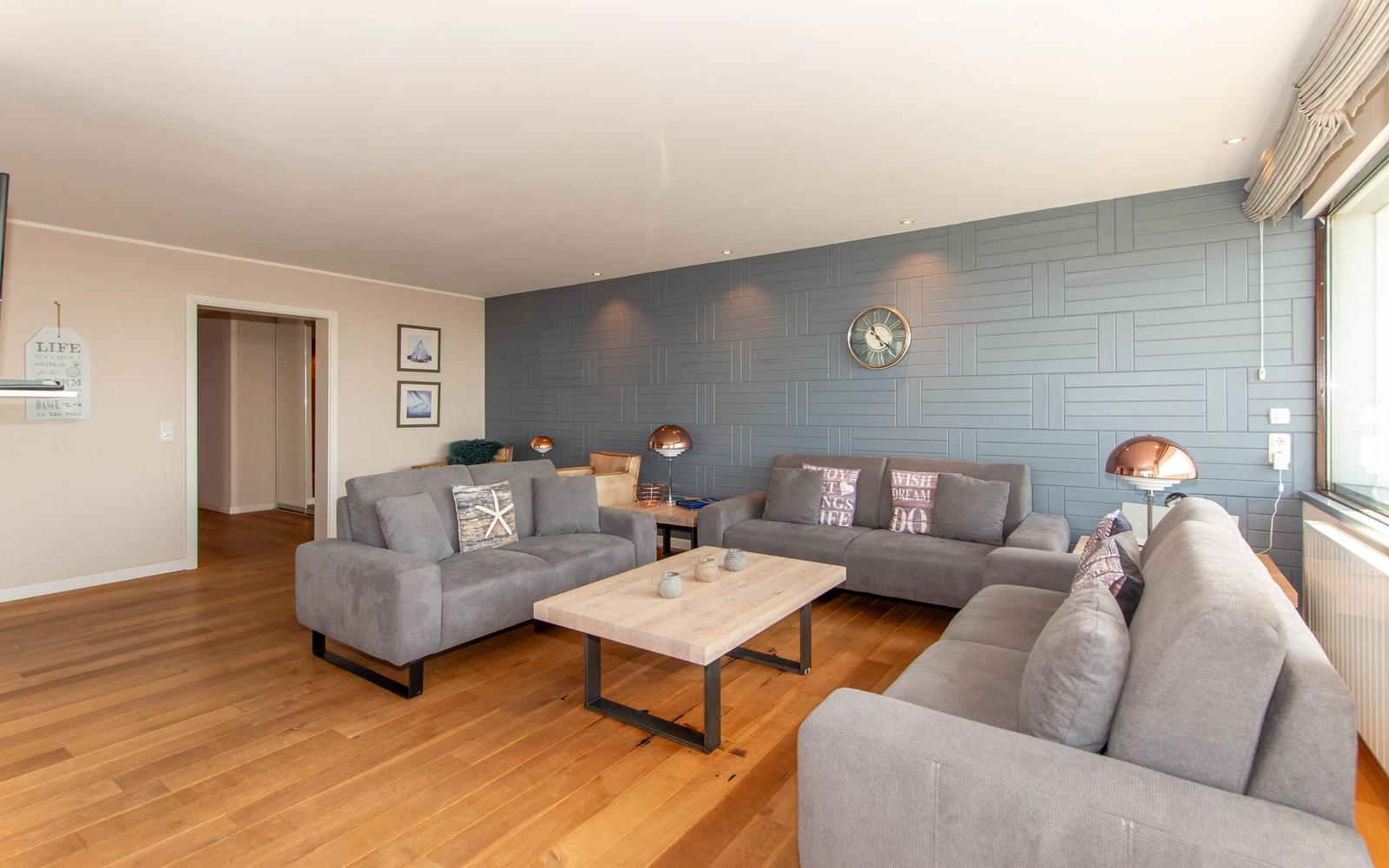 Wohnzimmer mit grauen Sofas, Holzboden und dekorativer Wand