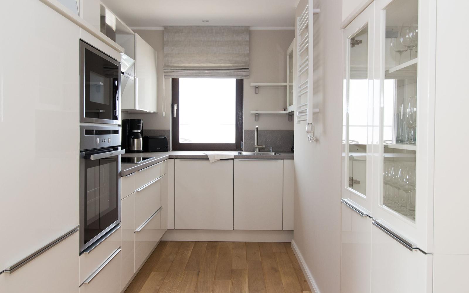 Küche mit weißen Schränken, Edelstahlgeräten und Holzboden.