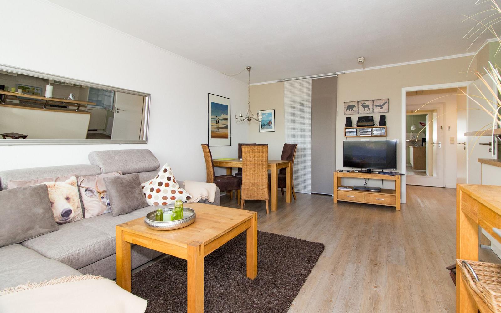 Wohnzimmer mit Sofa, Couchtisch und Fernseher. Essbereich mit Tisch und Stühlen. Holzboden und Spiegel an der Wand.