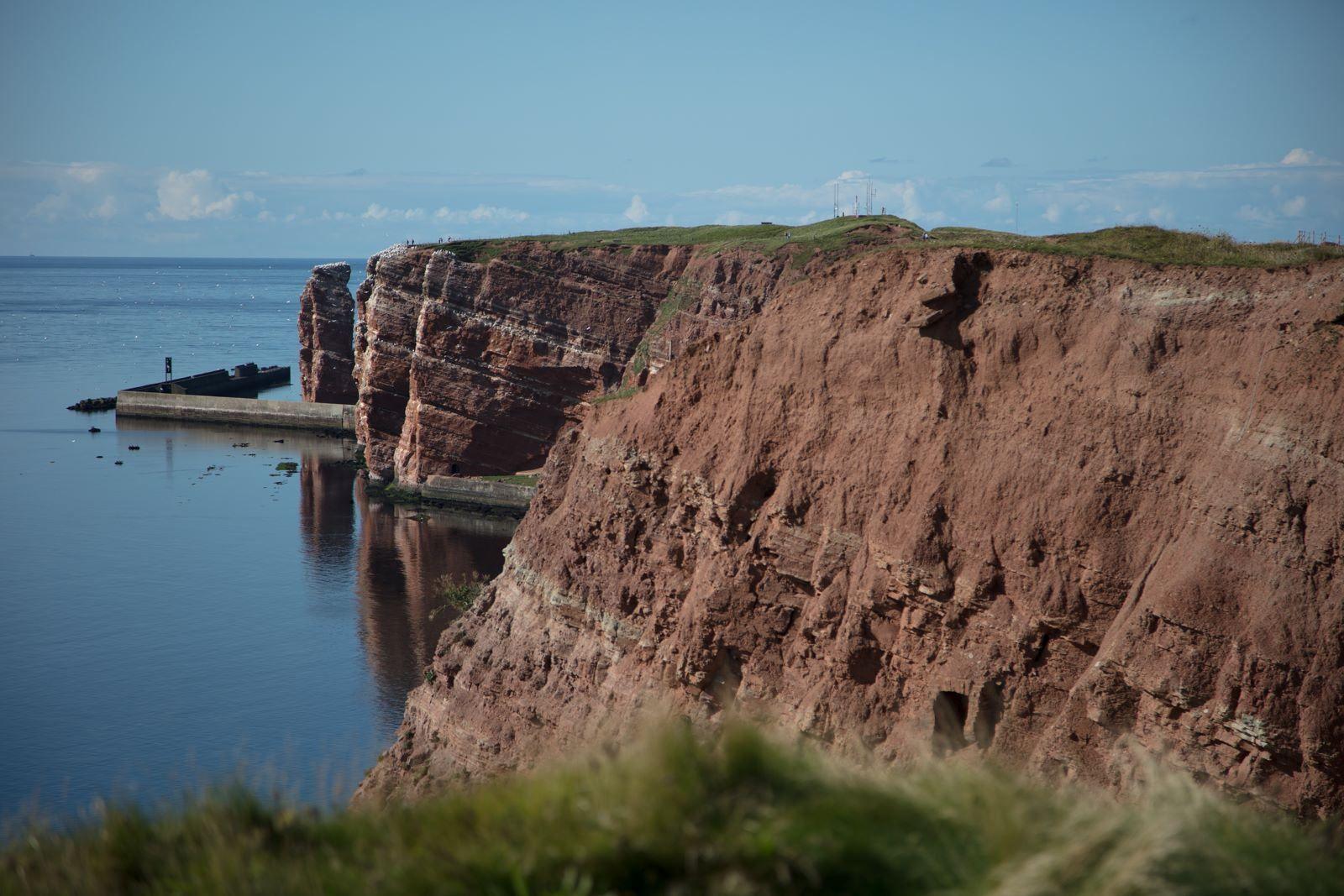 Rote Klippen am Meer mit Gras und Blick aufs Wasser.