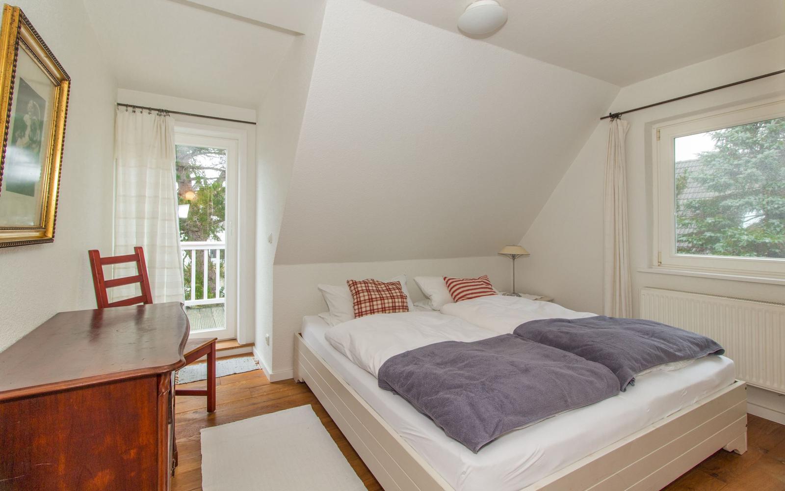 Schlafzimmer mit Doppelbett, Schreibtisch und Fenster zur Terrasse.