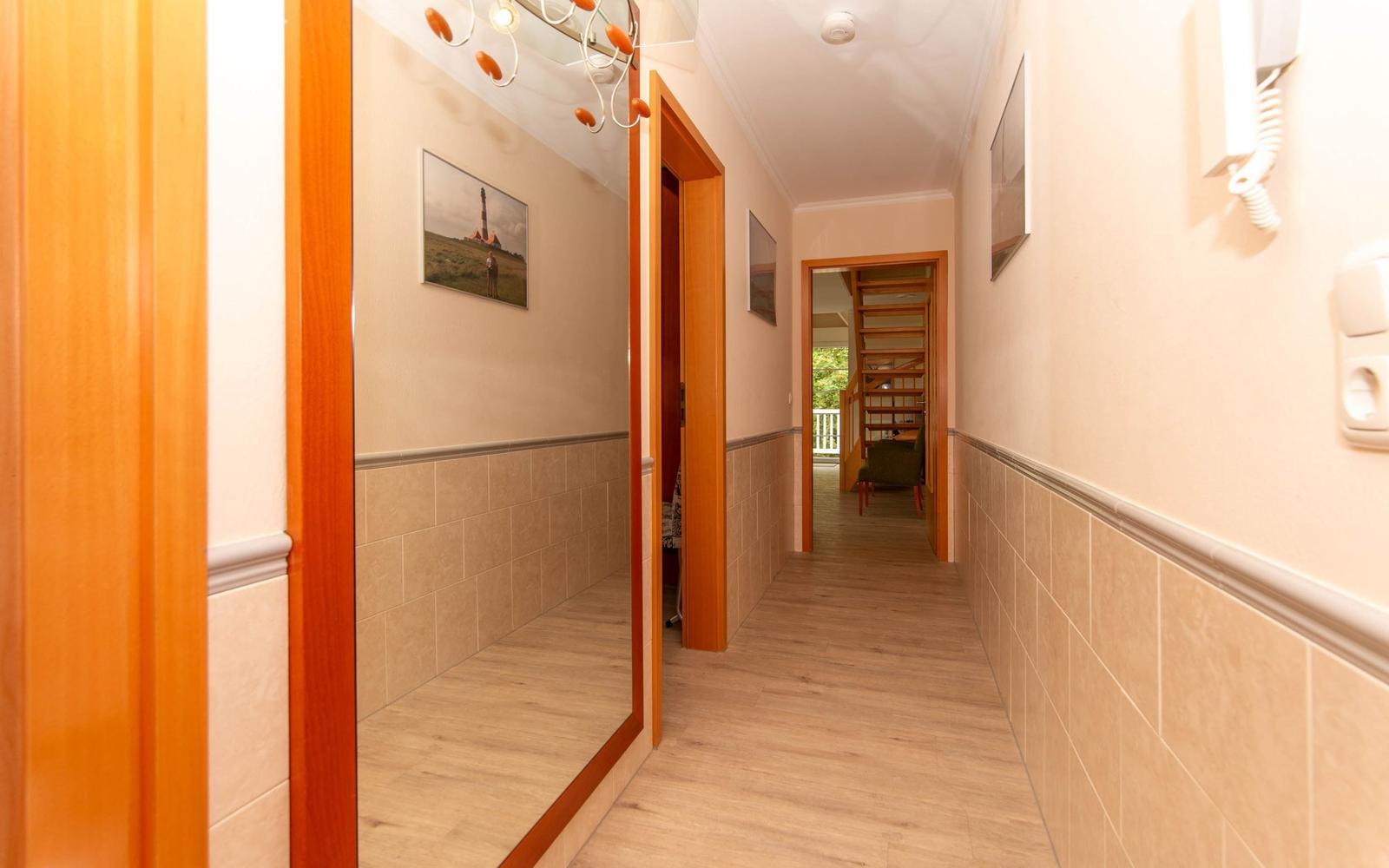 Flur mit Holztüren, Fliesen und Bildern an den Wänden.