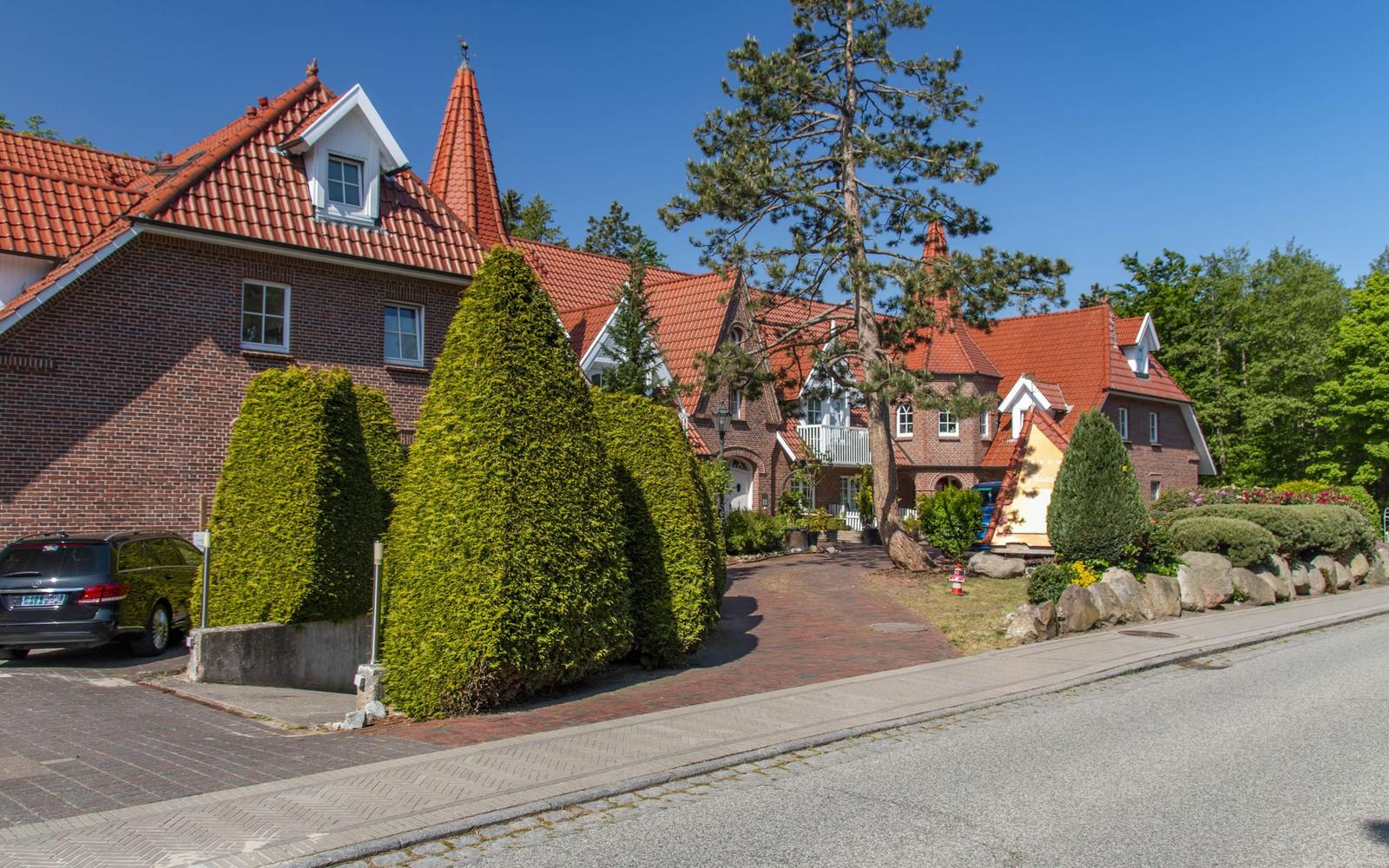 Haus mit rotem Dach und grüner Hecke an Straße
