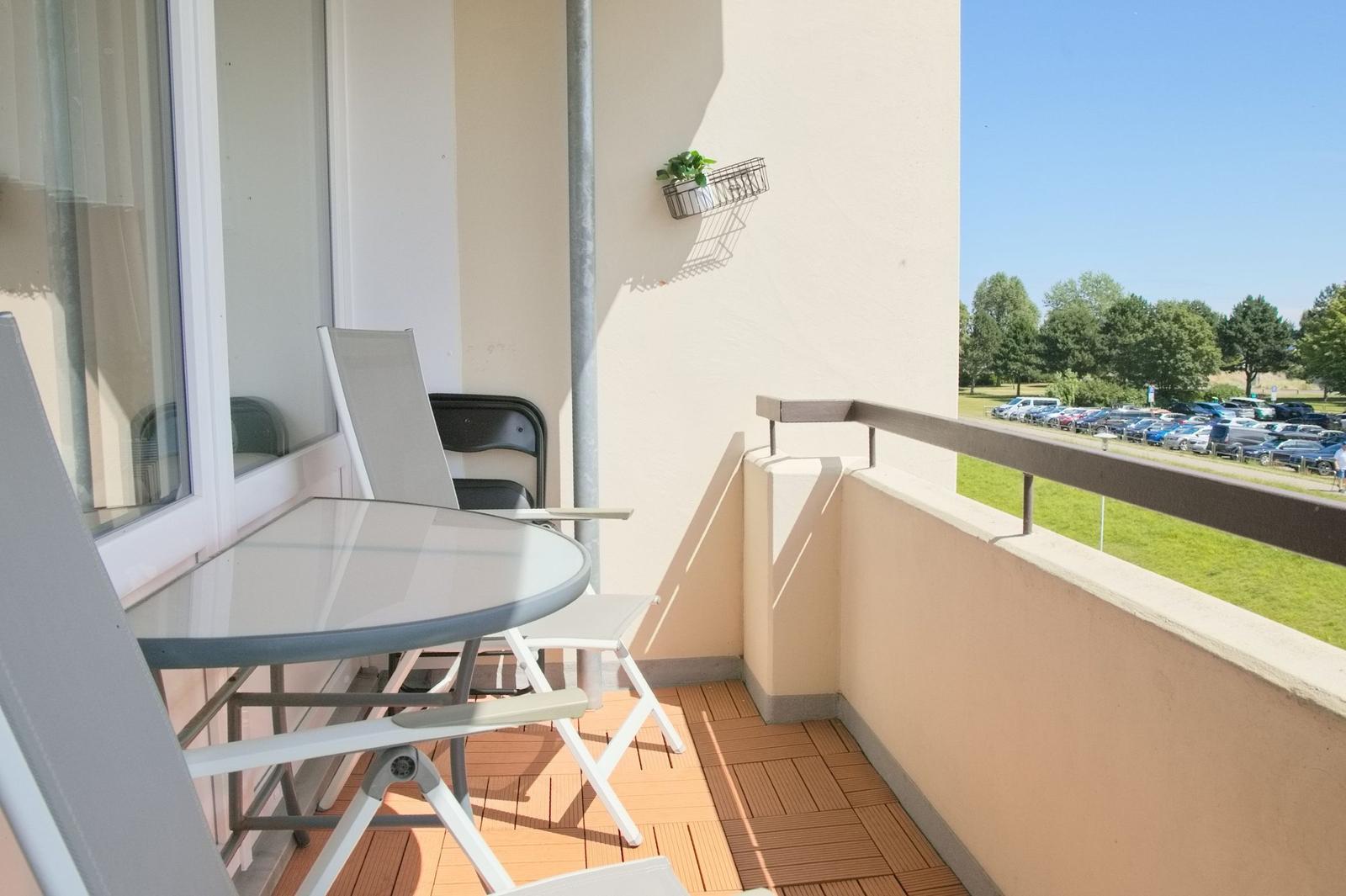 Terrasse mit Tisch und Stühlen, Blick auf Parkplatz und Grünfläche.