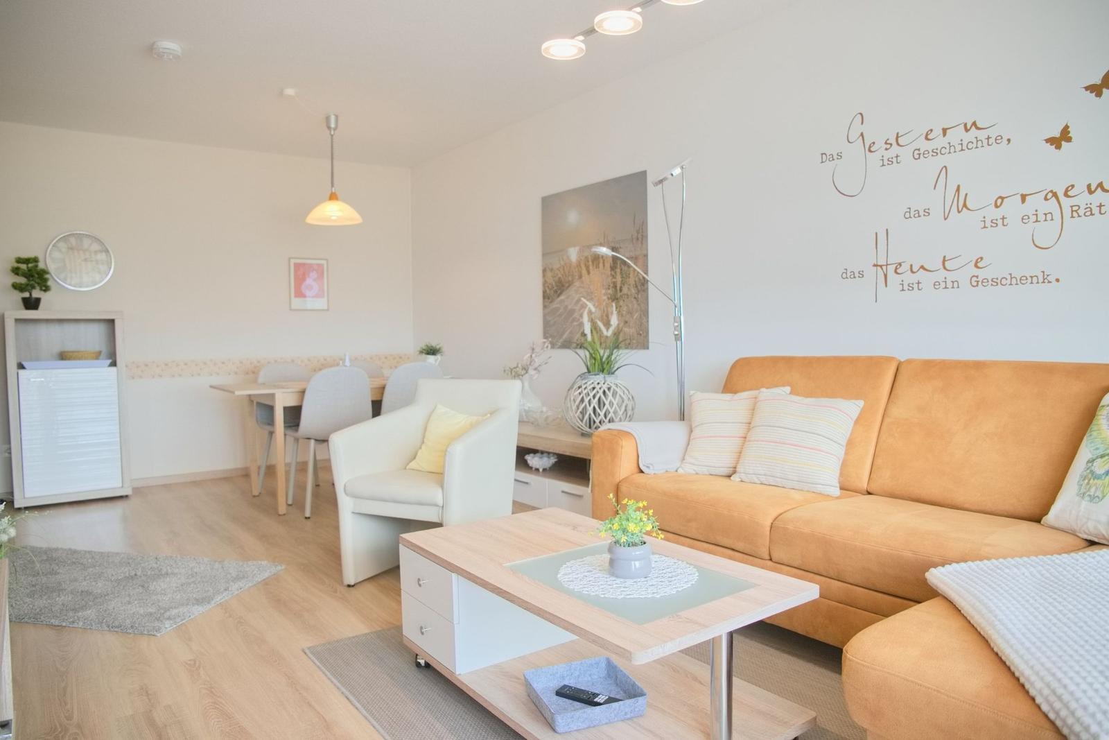 Wohn- und Essbereich mit Sofa, Tisch und Stühlen. Wanddekoration mit Zitat.