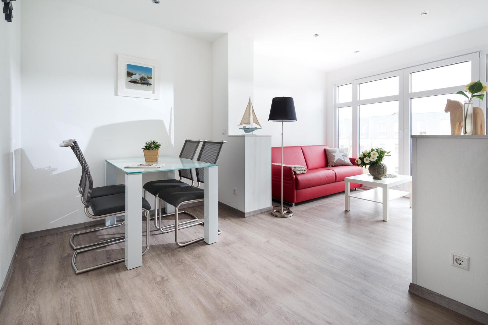 Wohn- und Essbereich mit rotem Sofa, Glas-Tisch und großen Fenstern.