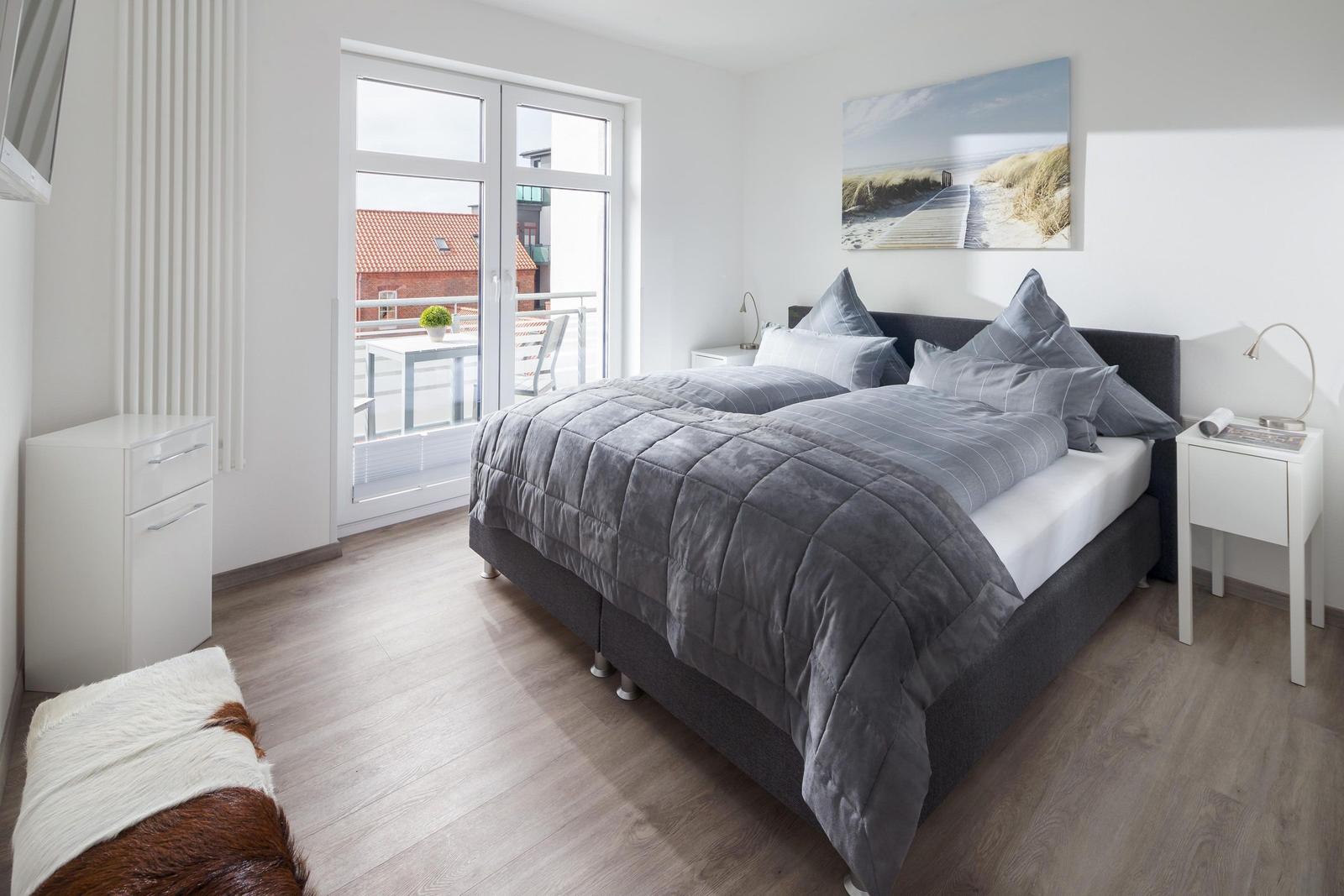 Schlafzimmer mit Bett, Nachttischen und Balkonansicht.