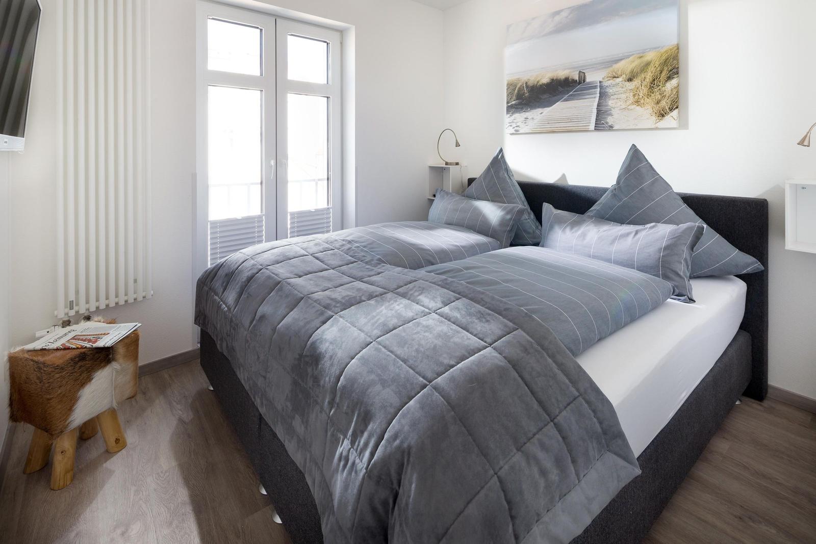 Schlafzimmer mit Doppelbett, Fenster und Wandbild.