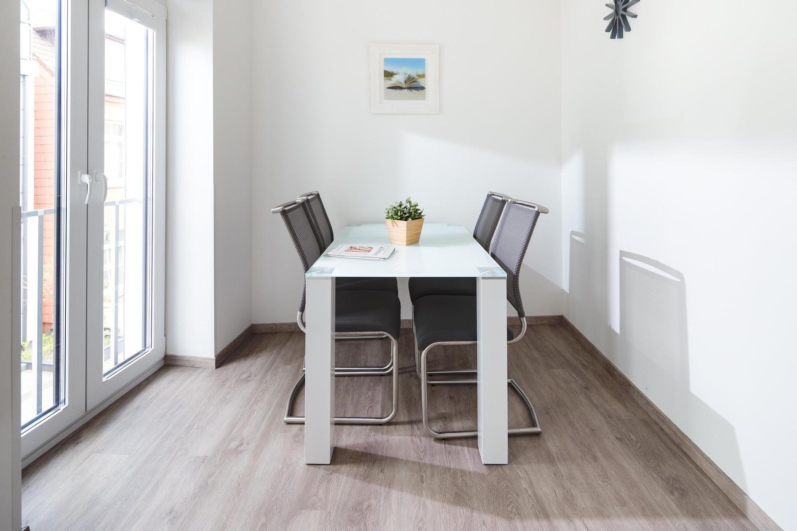 Essbereich mit Tisch und vier Stühlen, Glasplatte, Pflanze und Fenster.