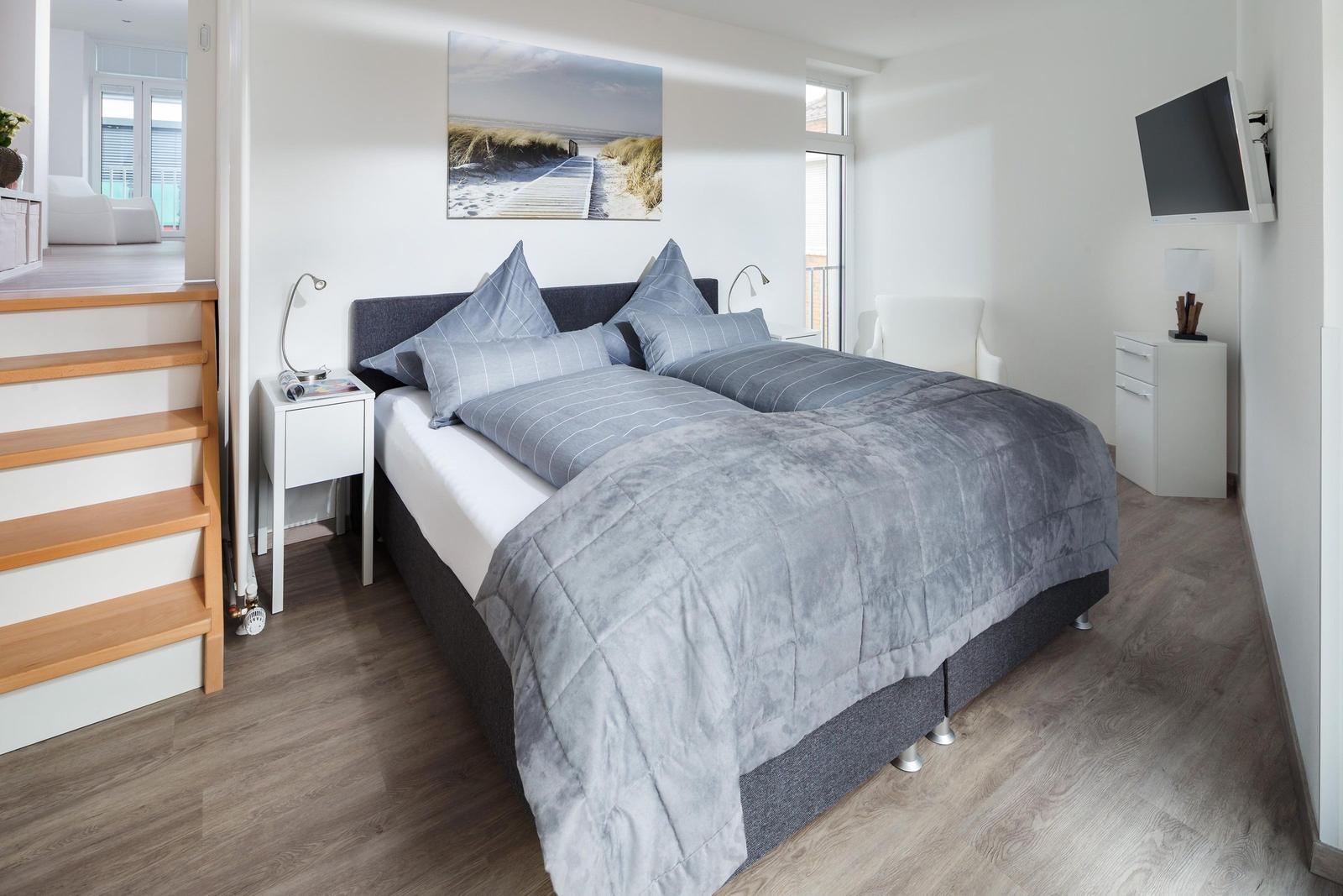 Schlafzimmer mit Doppelbett, Wandbild und TV. Holzstufen führen zu einer weiteren Ebene.
