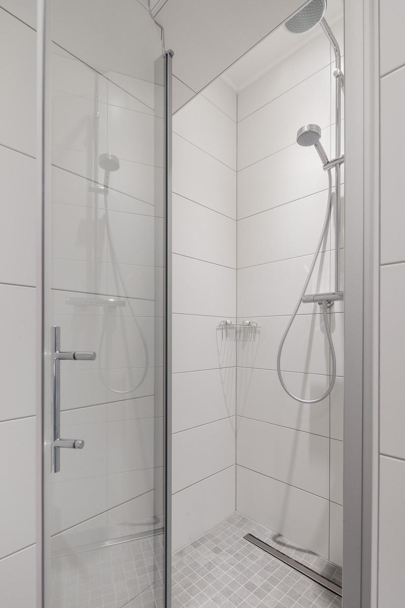 Duschkabine mit Glaswand, Duschbrause und Ablagekorb.