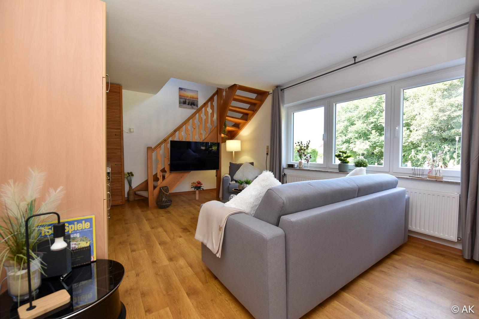 Wohnzimmer mit Sofa, TV und Holztreppe zur oberen Etage.