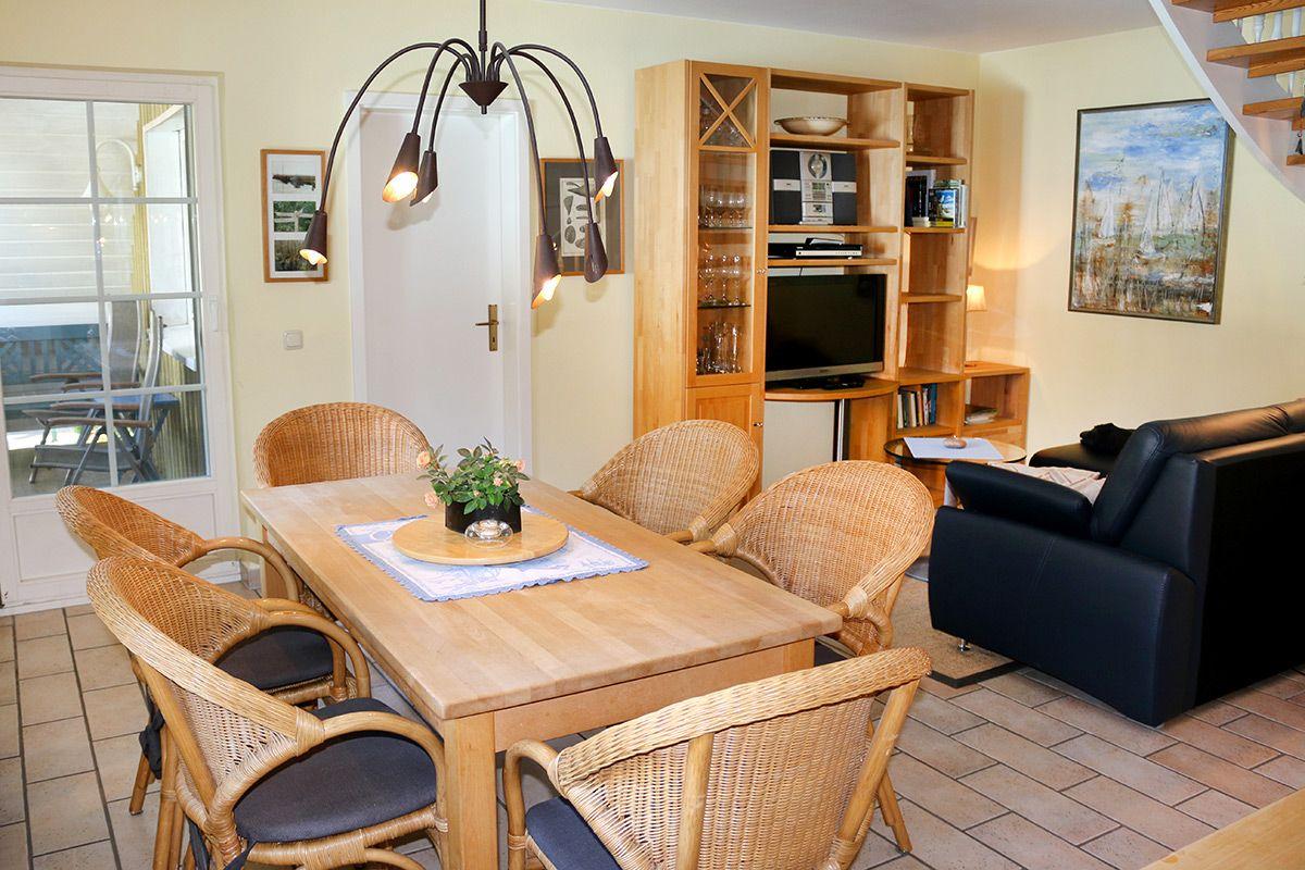 Esszimmer mit Holztisch, Rattanstühlen und integriertem Wohnbereich mit Sofa und TV.