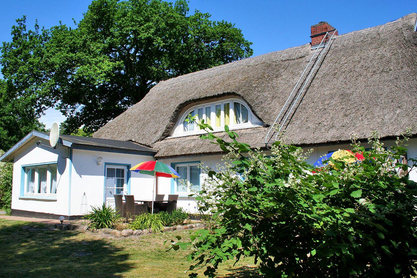 Haus mit Strohdach, Garten und Terrasse mit Sonnenschirm.