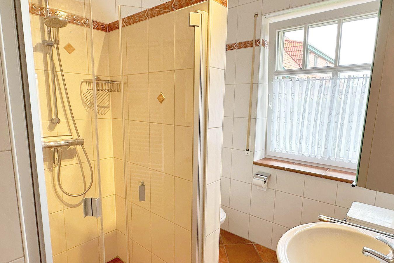 Bad mit Dusche, Waschbecken und Fenster mit Vorhang.