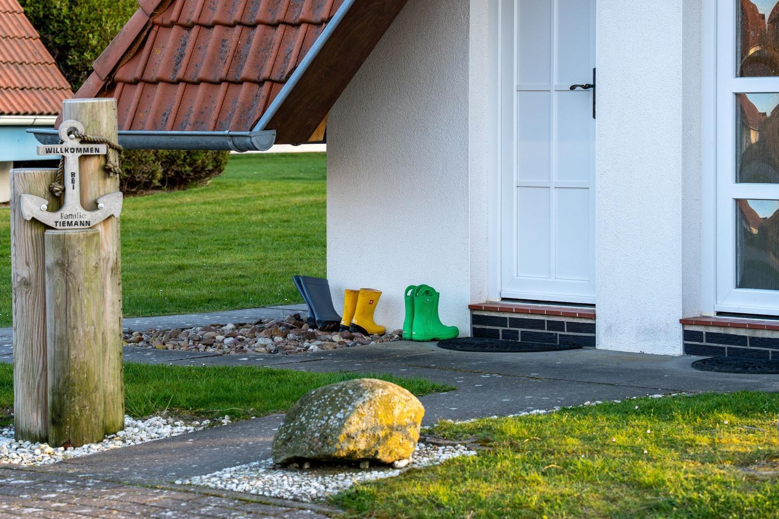 Welcome sign at entrance with rubber boots and stone path.
