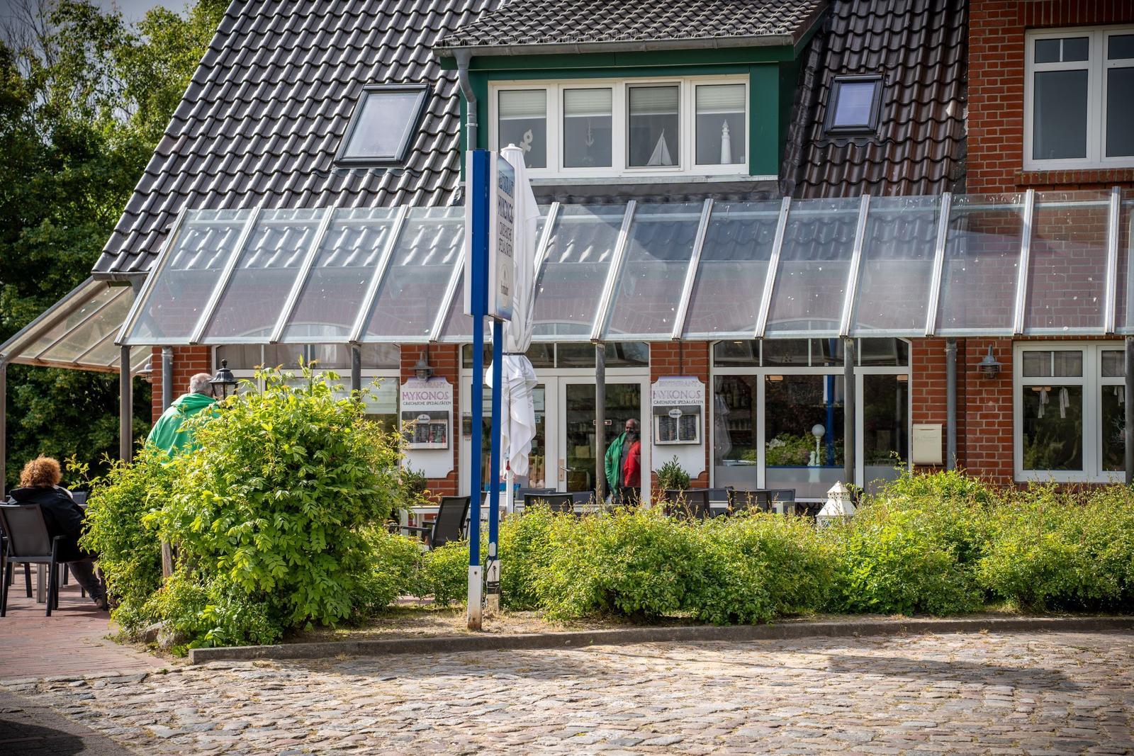 Guest house with glass roof, terrace, and green bushes in front of a cobblestone path.