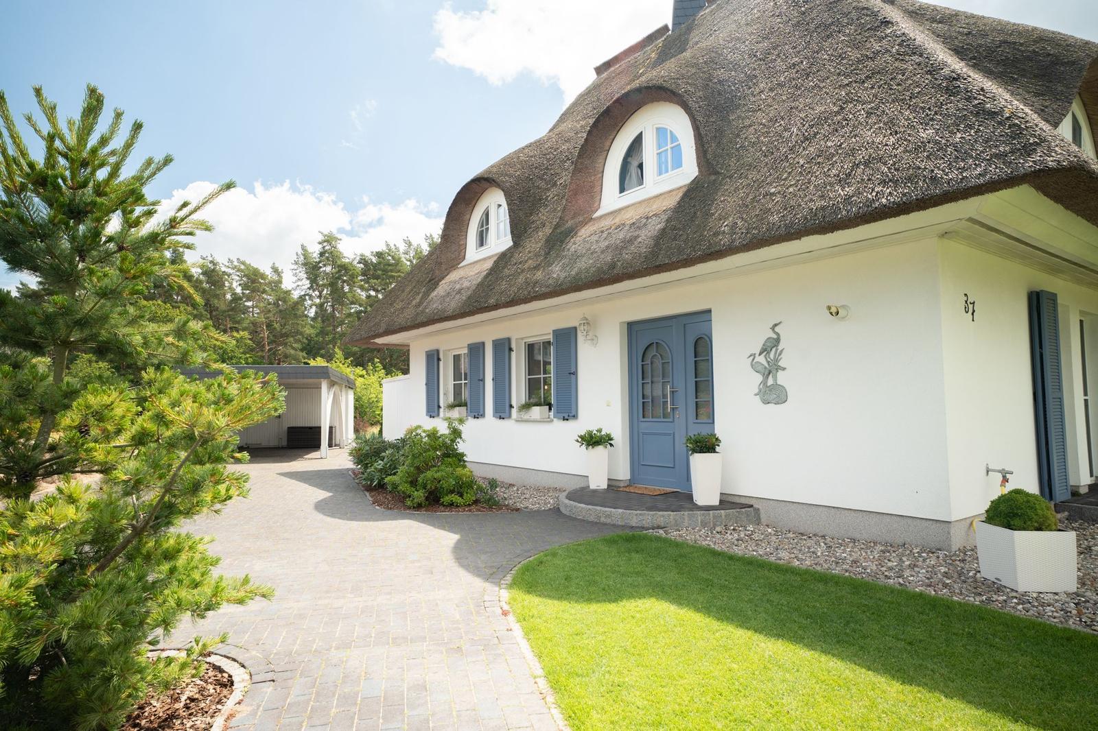Haus mit Strohdach, blauer Tür und blauen Fensterläden. Vorhof mit Rasen und Kiesweg.
