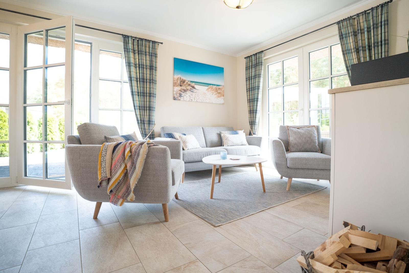 Wohnzimmer mit Sofa, Sesseln und Tisch. Fenster und Vorhänge sind sichtbar.