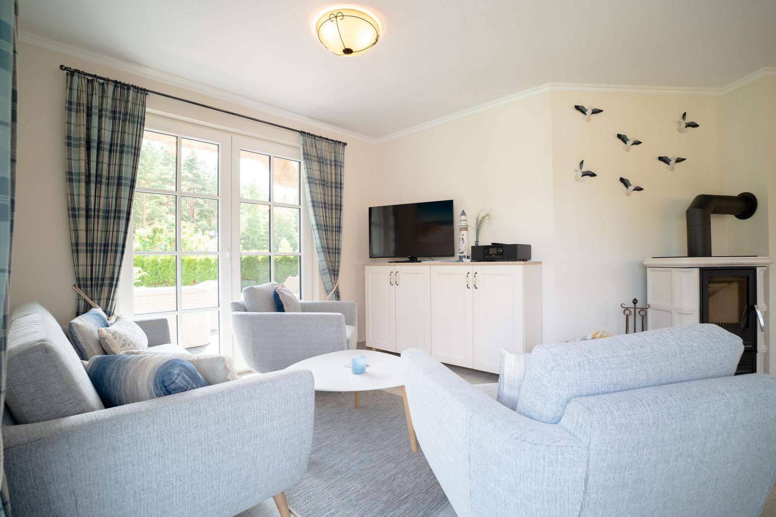 Wohnzimmer mit Sofa, Sessel und TV. Fenster mit Plaidgardinen. Kamin und Wanddekoration.