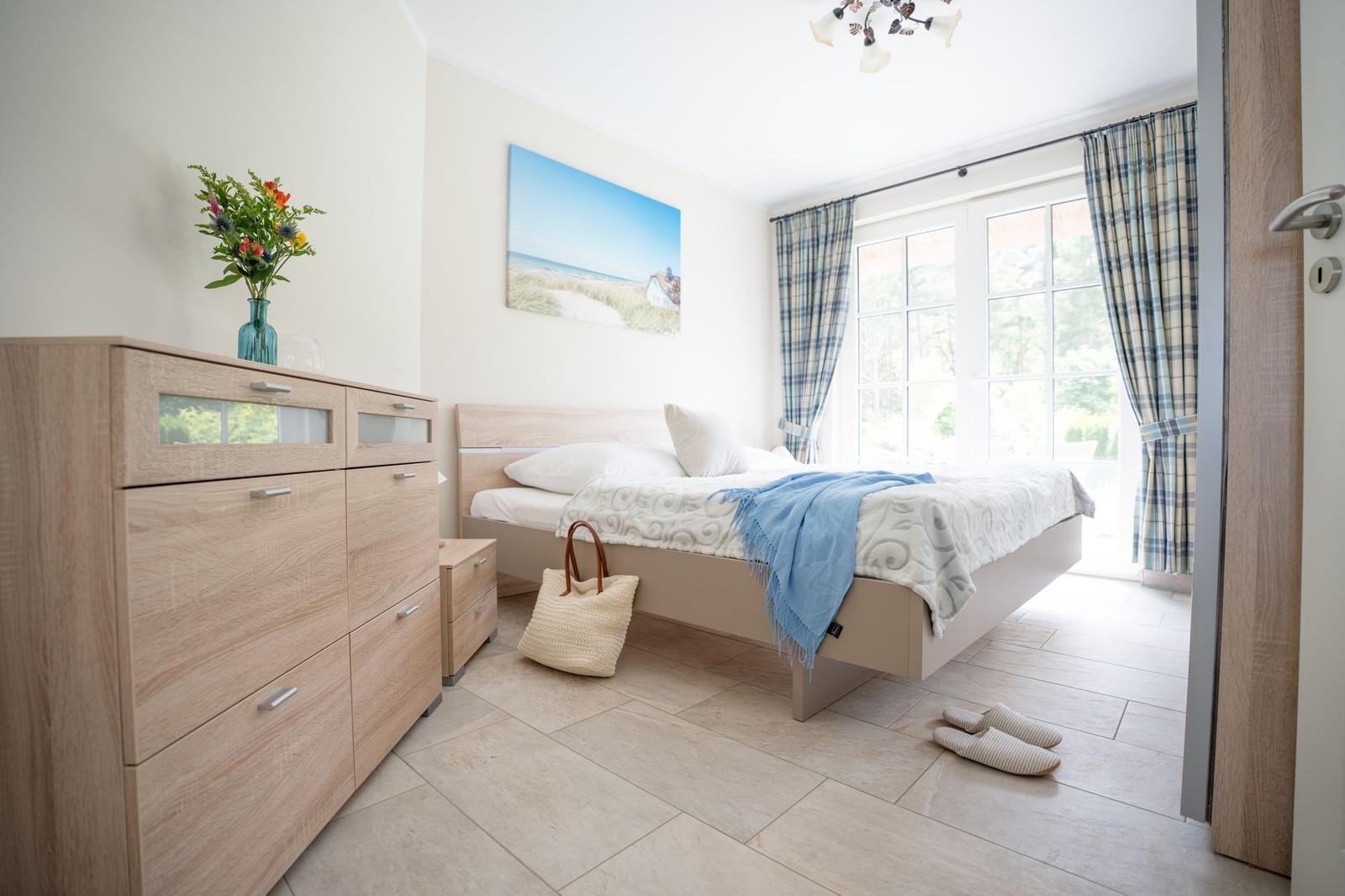 Schlafzimmer mit Bett, Schrank und Fenster mit Vorhängen.