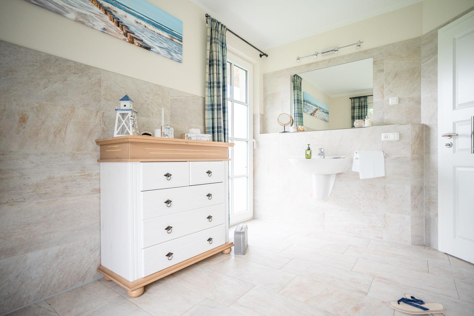 Badezimmer mit Waschbecken, Spiegel und Schrank. Fliesenwand und Boden.