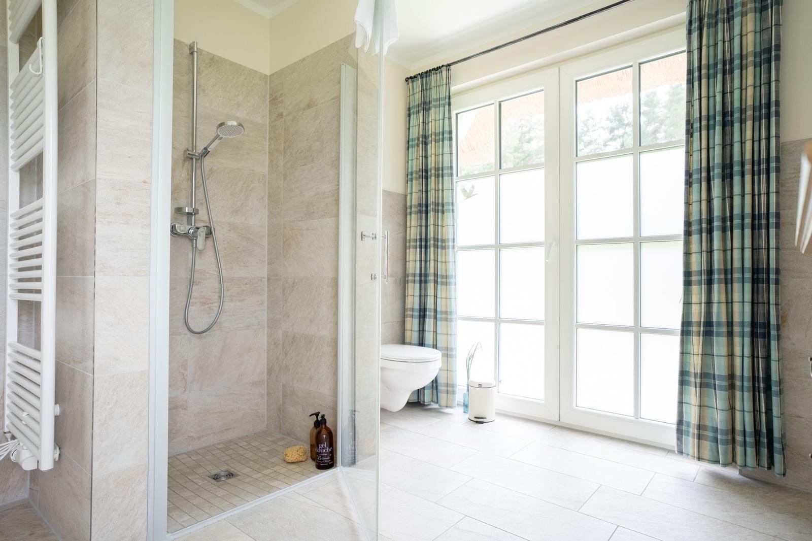 Badezimmer mit Dusche, Toilette und Fenster mit Vorhängen.