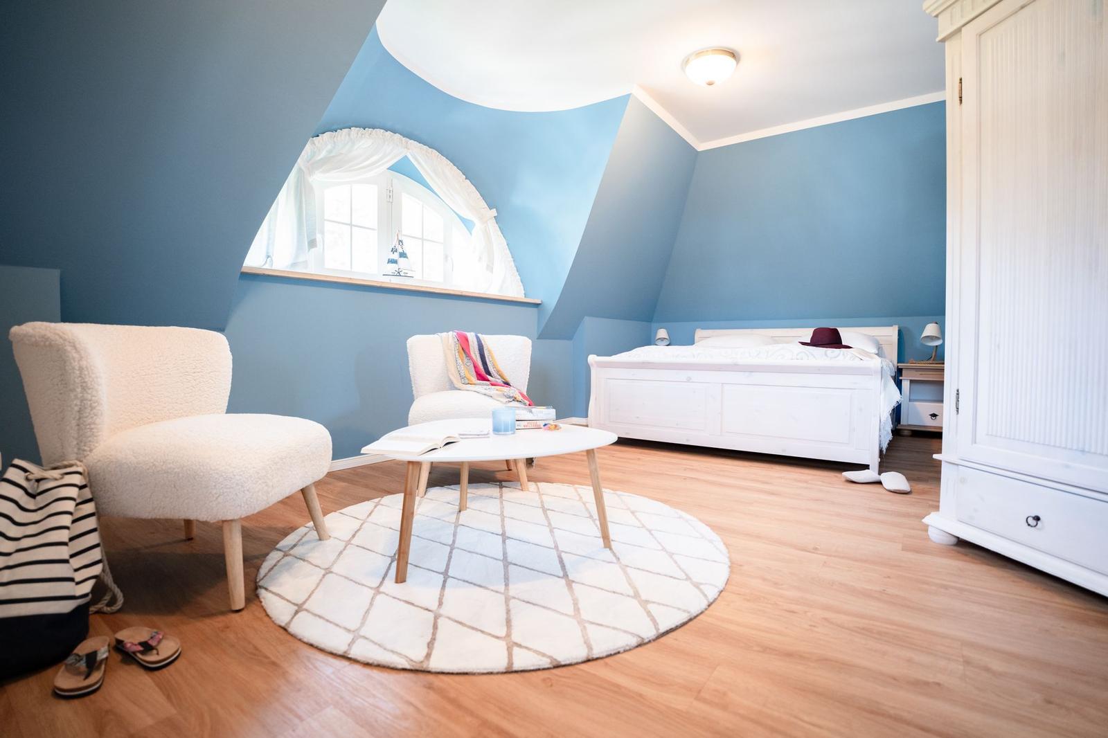 Schlafzimmer mit blauen Wänden, weißem Bett und Rundfenster.