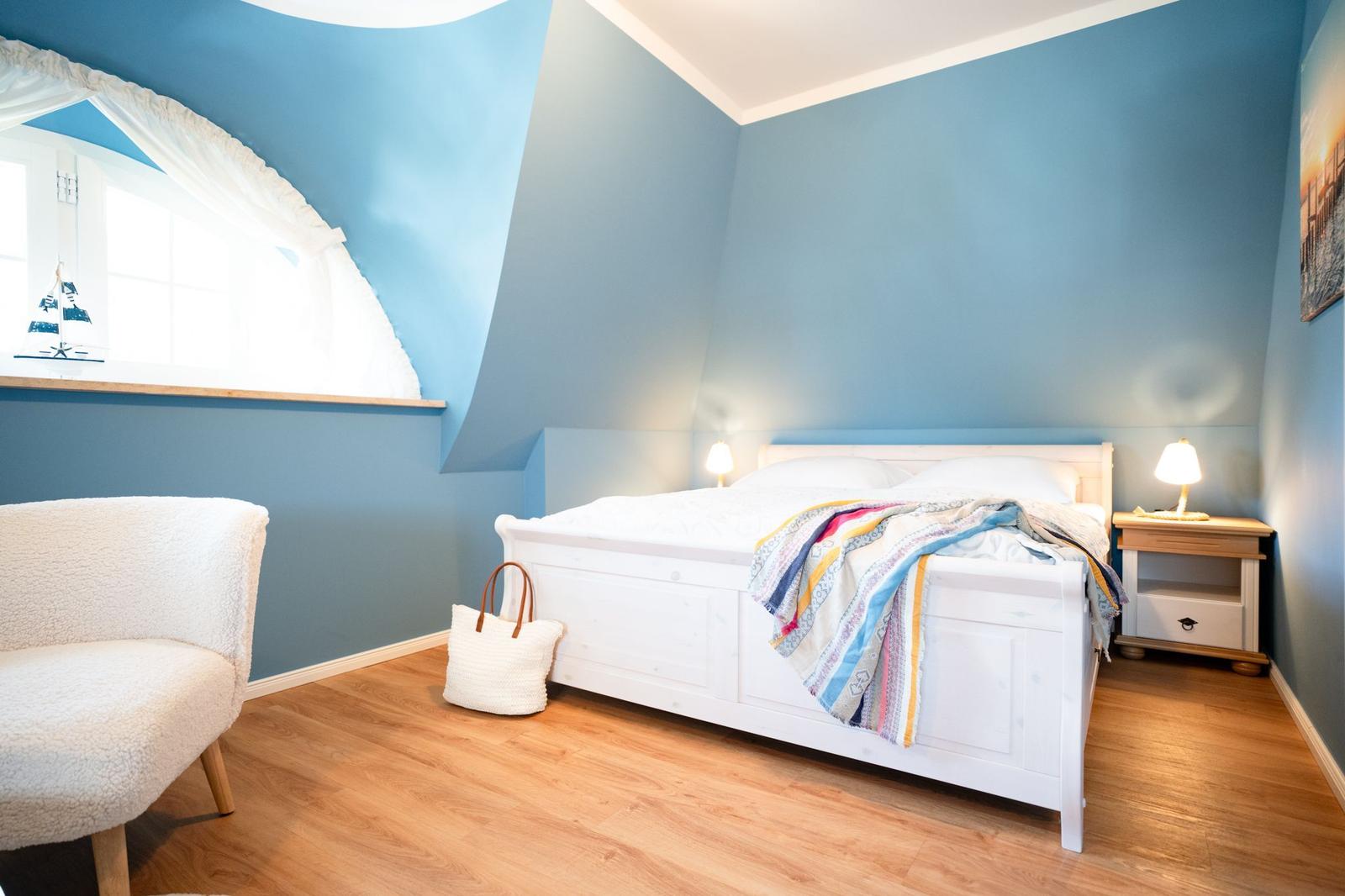 Schlafzimmer mit blauen Wänden, weißem Bett und Holzboden.